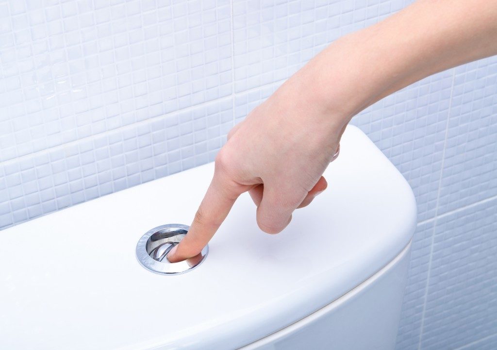 person pushing the flush button of a toilet