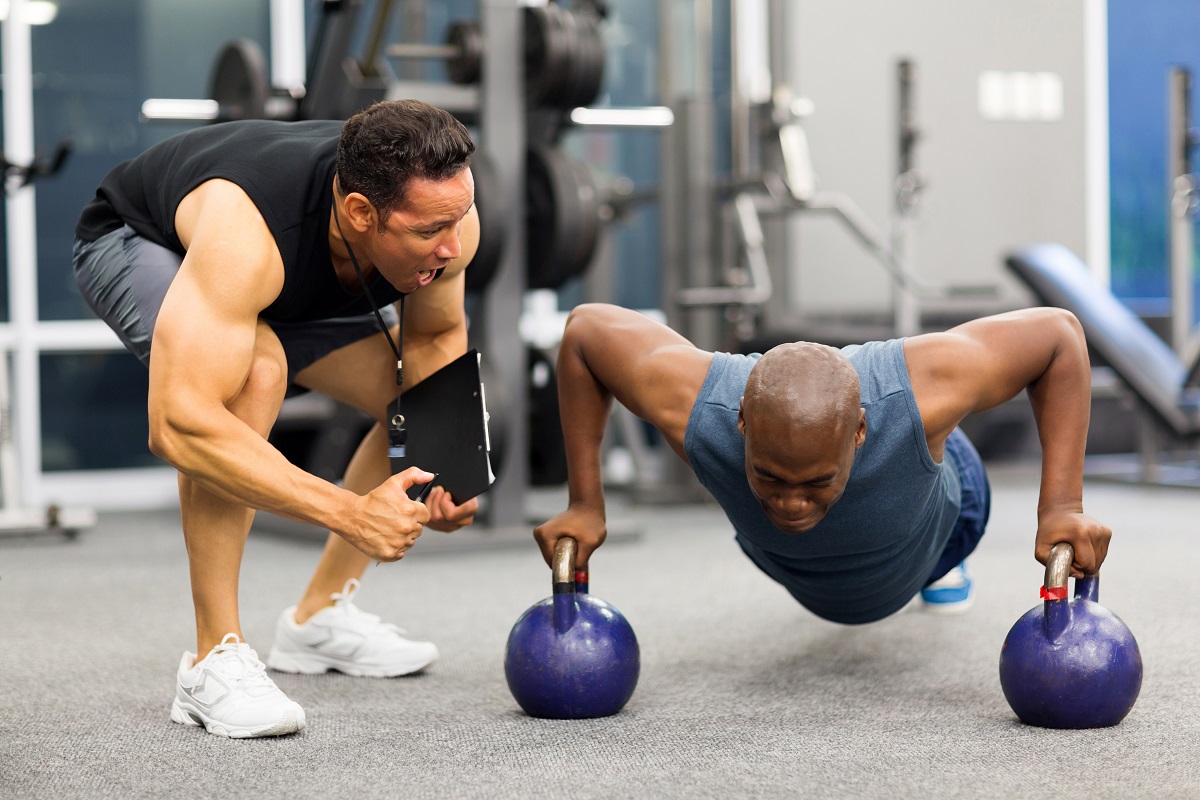 Man doing kettlebell pushups with trainer