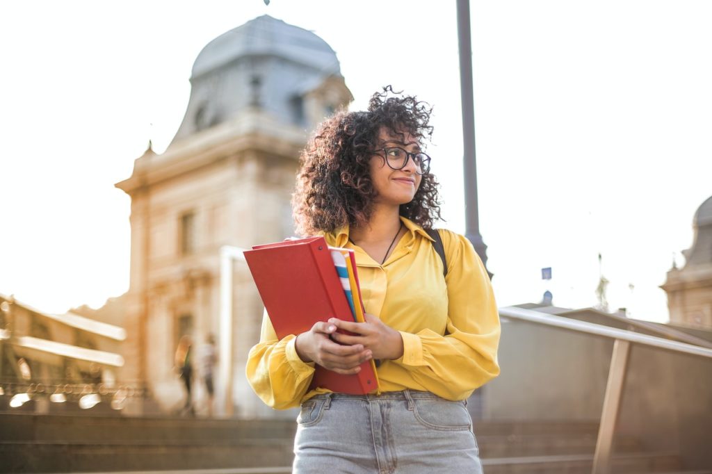 young woman holding books and binder in campus