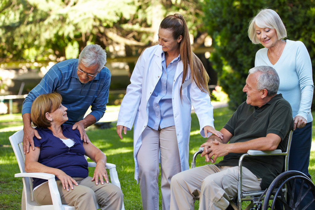 2 elderly people on wheelchair smiling with a doctor along with another 2 elderly people