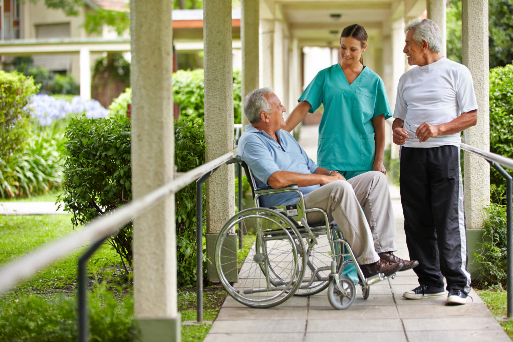 elderly man on wheelchair smiling with a nurse and another elderly man