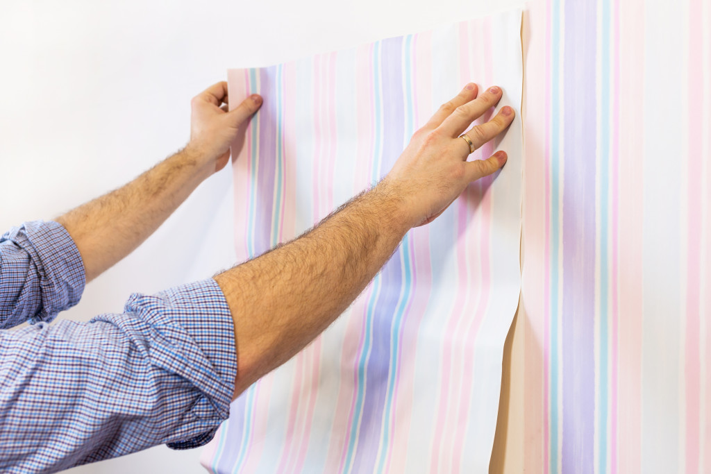 A person sticking colored wallpaper on white walls